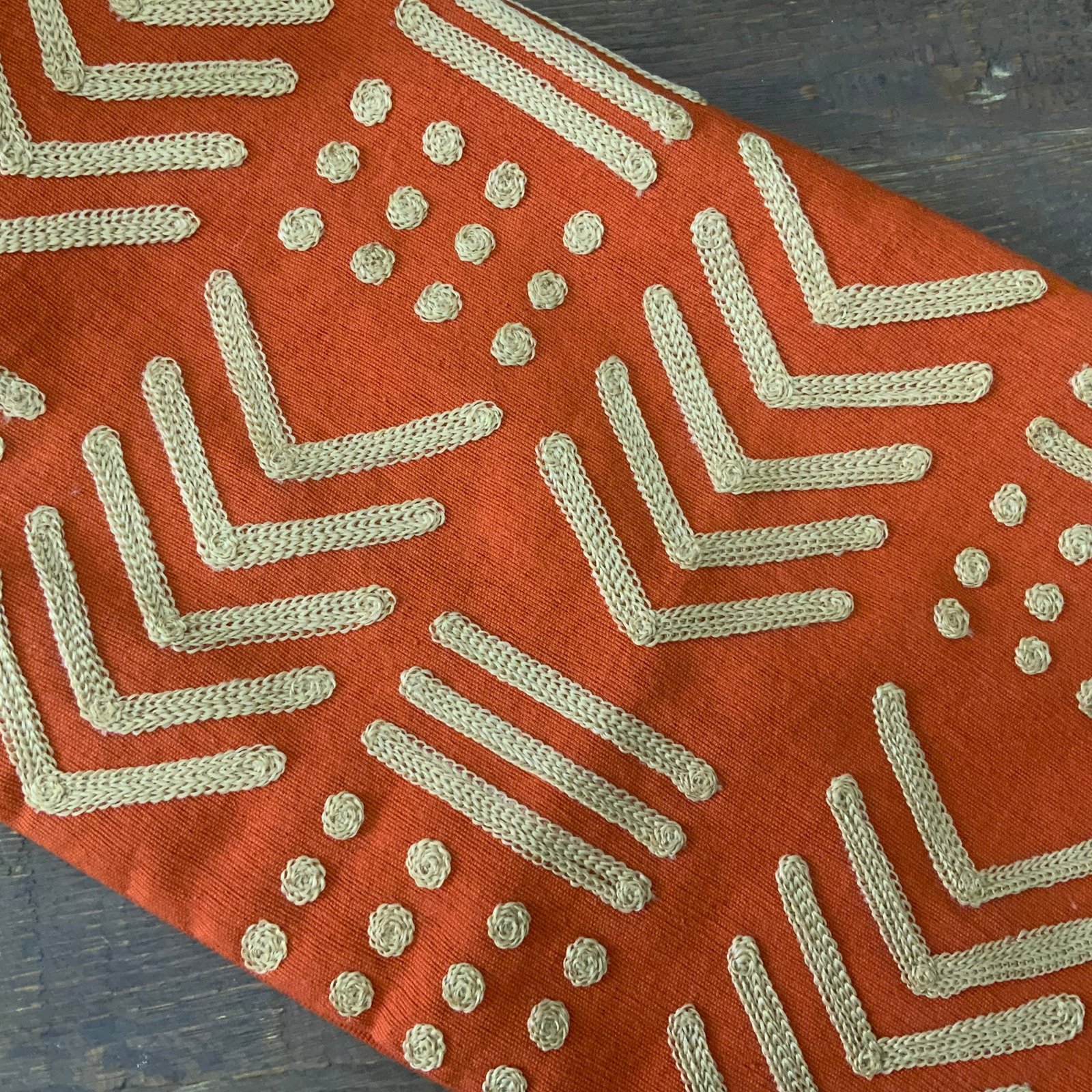 Square terracotta orange throw pillow cover with raised gold-toned geometric embroidery in a tribal mudcloth design featuring chevrons and dots.